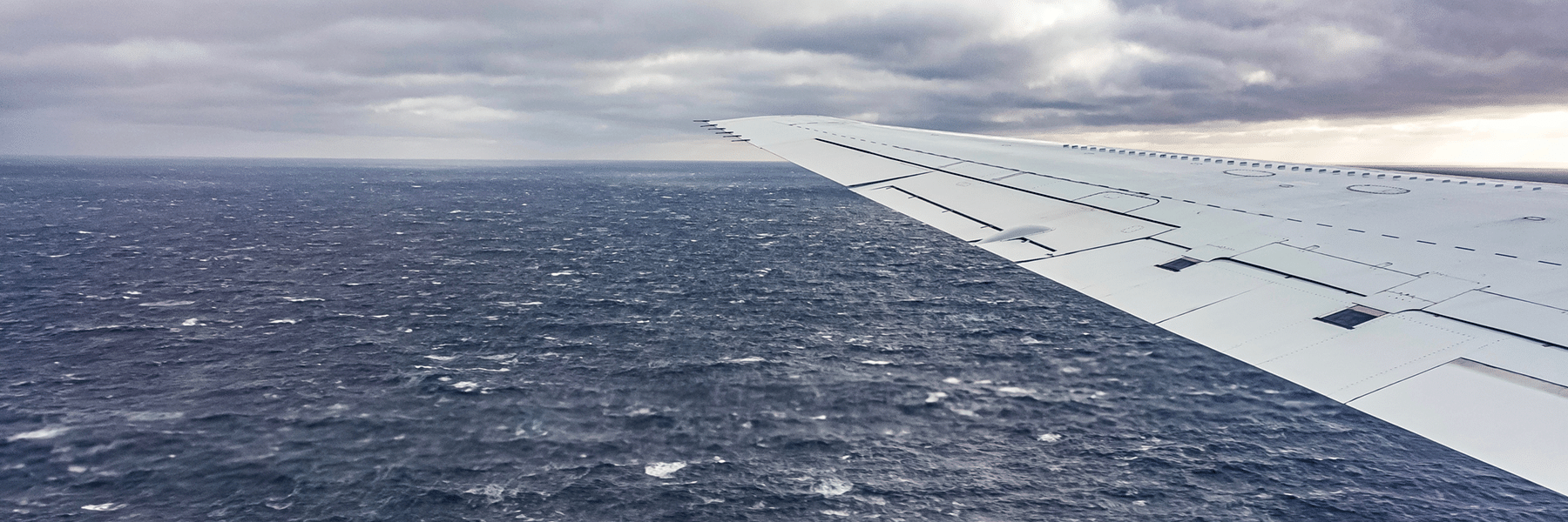 An airplane wing over the ocean with clouds in the background